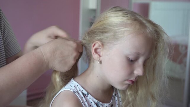 a mother braids a pigtail for a little girl, a mother's hands braid a pigtail for her daughter
