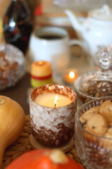Lit candles, cookies, chocolate, nuts, tea, wine, pumpkins, books, reading glasses and autumn leaves on the table. Autumnal hygge at home. Selective focus.
