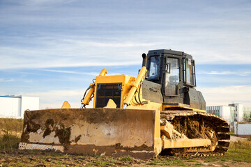 Yellow dirty excavator in career moves overburden. Bulldozer crawler combs the ground, with blue sky in the background, three quarter front view with copy space.