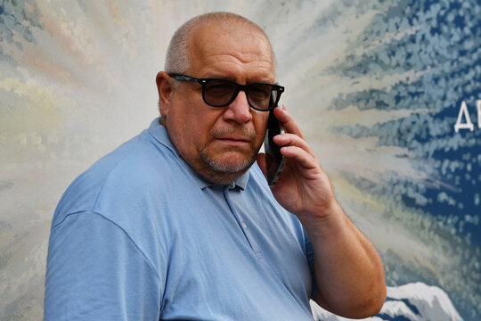 Portrait of Caucasian elderly gray-haired man with glasses talking on the phone.