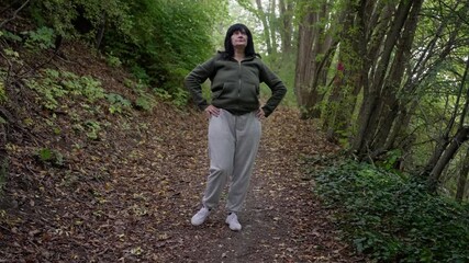 selfassured woman on forest trail, female explorer standing confidently along woodland path, caucasian woman with hands on hips displaying outdoor leadership and adventurous spirit amidst trees