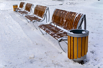 A row of benches sitting next to a trash can in the snow
