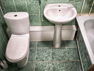 Modern bathroom with green tiles showcasing sink, toilet, and tub in a small space