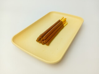 Chocolate biscuit stick served on a square plate, isolated on white background.