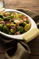 Close up of roasted brussels sprouts with bacon in dish on wooden surface