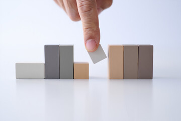 Hand placing neutral colored wooden block into structure, symbolizing balance, construction, strategy, or progress on white background