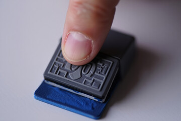 Close-Up of a Gray Stamp Being Pressed Onto an Ink Pad by a Finger on a White Surface Creating Graphic Design