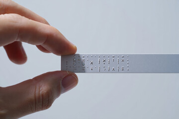 Hand Holding a Silver Metal Bar with Etched Symbols and Perforations on White Background for Technical or Industrial Purposes
