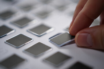 Person Picking Gray Metallic Labels from Matrix on White Background Close Up in Studio for Creative Composition 150 Characters