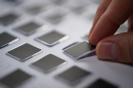 Person Picking Gray Metallic Labels from Matrix on White Background Close Up in Studio for Creative Composition 150 Characters