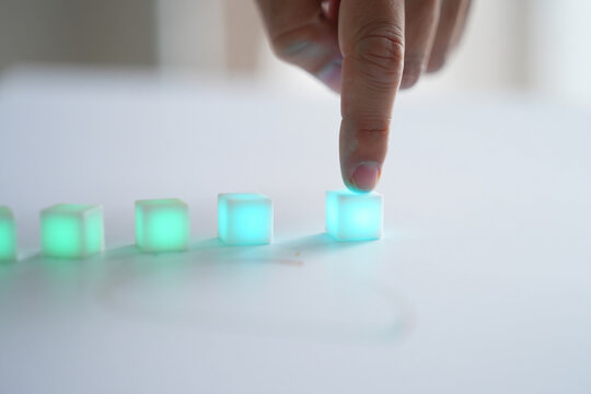Index Finger Pushing on Lighted Blue Cube on White Background with Row of Cubes 150 Characters