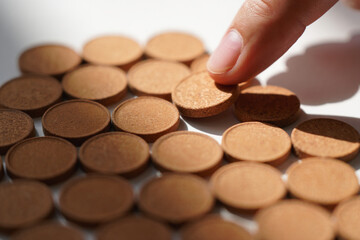 Hand Picking Brown Round Pills on White Surface Concept of Medicine Healthcare Treatment Remedy and Pharmaceutical Industry 150 Characters