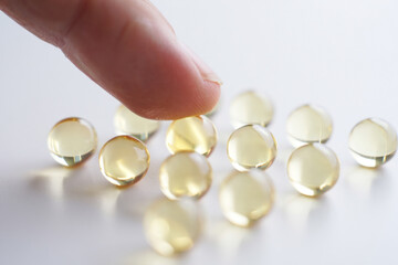 Finger Touching Group of Round Gel Capsules on White Surface Health Supplements Vitamins Nutrition Healthcare Medicine Pharmaceutical Industry