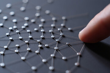 Nails and string art installation represents connected dots concept with finger touching web of connections on dark grey