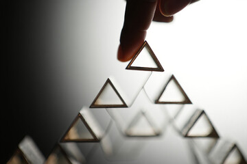 Human Hand Putting Triangle on Top Layer of Triangle Stacked Construction Concept Close up Shot with Selective Focus on Gradient Background