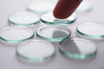 Human Finger Placing Glass Lens on Top of Others Lying Flat on White Surface Demonstrating Selection Concept Close up Shot with Selective Focus