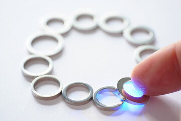Hand Adds Ring to Circle of Rings with Blue Light Underneath for Creative Puzzle or Completion Metaphor Concept 150 Characters