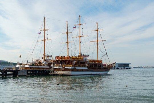 Two majestic two-masted pleasure sailing ship docked at pier of embankment of Gelendzhik, with tall masts and Russian flag, set against calm Black sea.  Gelendzhik, Russia - December 14, 2022