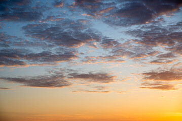 The sky is painted with vibrant colors as the sun sets, casting a warm glow on fluffy clouds. This tranquil scene captures the beauty of nature in the evening light