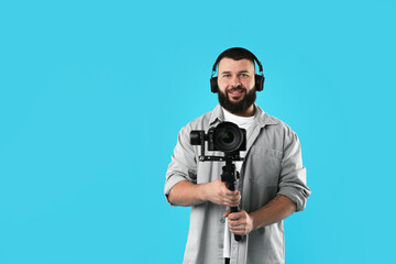 Videographer using gimbal stabilizer with camera on light blue background. Space for text © New Africa