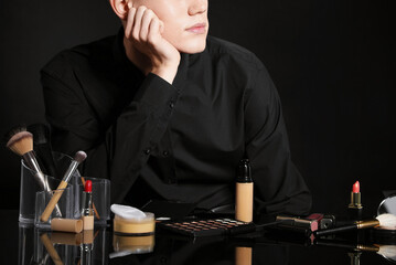 Makeup artist with tools and cosmetic products at table on black background. Space for text