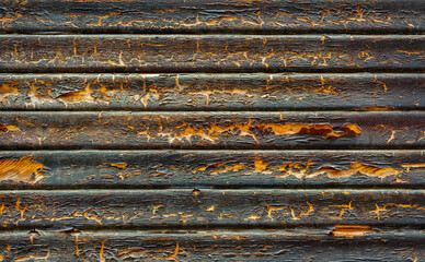 Close view of a weathered wooden surface with deep grooves and peeling paint. The colors vary from black to warm brown, illustrating years of exposure to elements