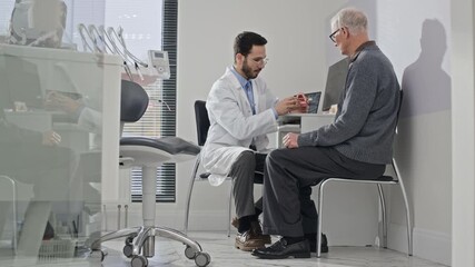 Male dentist showing dental model to senior patient during consultation in bright contemporary clinic focused on oral health guidance - Powered by Adobe