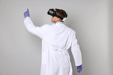 Modern technology. Doctor using virtual reality headset on light grey background, back view