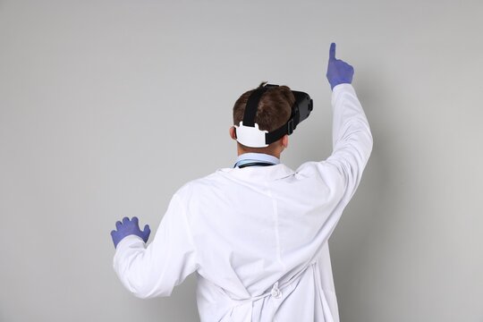 Modern technology. Doctor using virtual reality headset on light grey background, back view