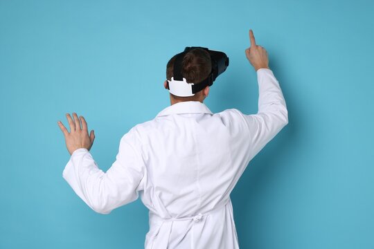 Modern technology. Doctor using virtual reality headset on light blue background, back view