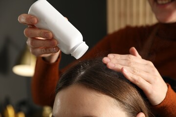 Naklejka premium Hairstylist applying talcum powder onto woman's hair at salon, closeup