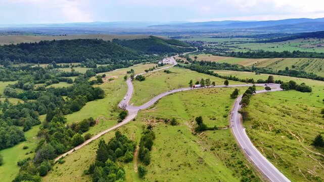 Curved country road across open green hills. A long rural road winds through rolling grassy hills and scattered farmlands.