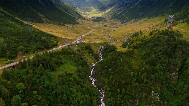 Mountain valley with long waterfall and road. A tall cascading waterfall drops through a deep green valley beside the winding road.