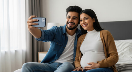 A happy young couple takes a selfie together at home, with the woman lovingly holding her pregnant belly.