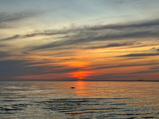 Vibrant sunset over calm sea with dramatic orange and gray clouds. Reflection of sun creating golden path on water surface. The view is peaceful and vast.