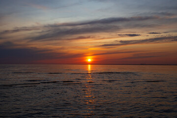 A serene sunset casts warm orange and red hues across the sky and water. Gentle waves reflect the sun fading light on the tranquil horizon. Golden hour at the beach.