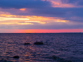 Scenic sunset over body water. The sky is painted with bright colors. Dramatic cloudscape.  Cloudy summer evening.