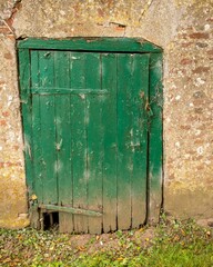 Old damaged green wooden door in a weathered wall with padlock and chain