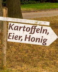 Wooden sign pointing to potatoes, eggs, and honey in german