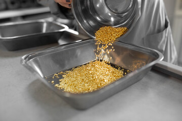 Golden popcorn kernels cascade into a stainless steel tray, creating a textured pile of deliciousness.