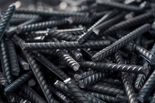 A pile of dark, twisted rebar fills a close-up frame with industrial texture. - Powered by Adobe