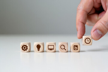 Hand Placing Wooden Cube with Clock Icon on Row of Other Cubes with Gear Bulb Computer Magnifier Blog Symbols on Table Concept