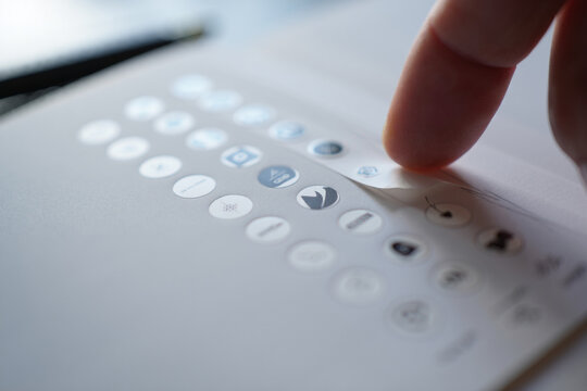 Finger Peeling Sticker from Sheet with Web Design Graphic Symbols on White Surface for User Interface Improvement Concept Development