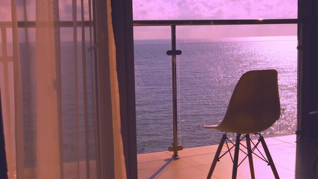 Beautiful Relaxing Ocean View from the Patio Window of a Beachfront Real Esrate at Brigrt Colorful Sunset Sky Clouds Sun Transparent Curtain Iridescent Water in the Sea Beach. Luxury Morden Room Chair