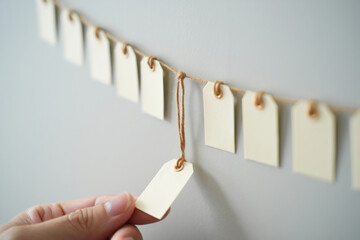 Blank Tags or Labels Hanging From String Held by Hand Isolated Against Gray Background Promotion Sale Design Creative Style Discount