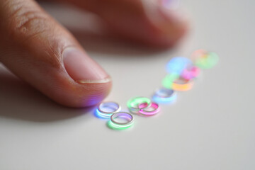 Hand Close-Up Presenting Small Silver Jump Rings with Vibrant Neon Light Reflection on Tabletop Displaying Jewelry Design and Craftsmanship