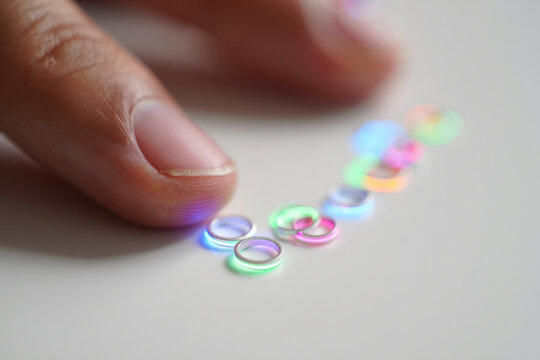Hand Close-Up Presenting Small Silver Jump Rings with Vibrant Neon Light Reflection on Tabletop Displaying Jewelry Design and Craftsmanship