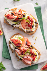 Delicious open-faced sandwich topped with fresh figs, prosciutto, and drizzled balsamic on a white marble surface