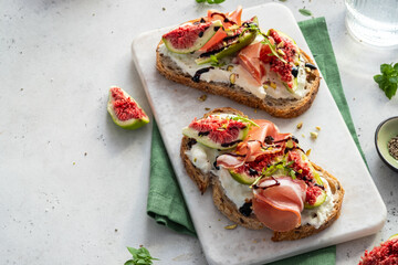 Delicious open-faced sandwich topped with fresh figs, prosciutto, and drizzled balsamic on a white marble surface