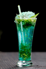 Vibrant turquoise blue cocktail or mocktail in a tall glass, richly infused with fresh green mint or cilantro and garnished with a paper umbrella. A refreshing, tropical, and cooling summer drink.